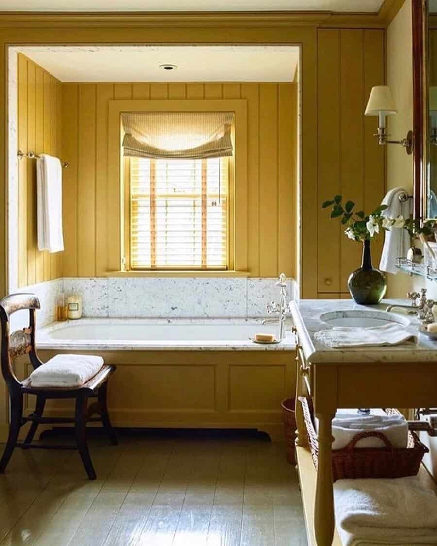 Bathroom with soft yellow paneling, marble bathtub, vintage sink, and natural light for a warm, inviting feel.