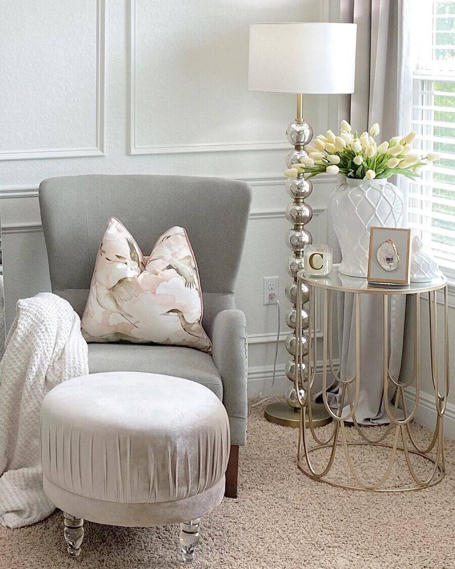 Bedroom sitting area with a plush armchair, velvet ottoman, gold-accented side table, and soft neutral decor.