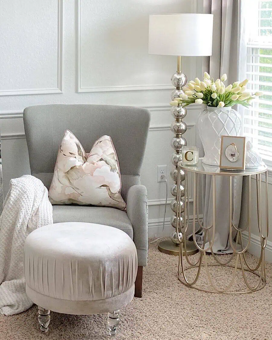 Bedroom sitting area with a plush armchair, velvet ottoman, gold-accented side table, and soft neutral decor.