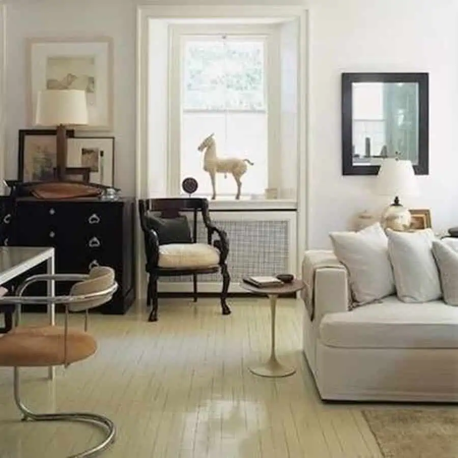 Living room with cream painted wood floor, white sofa, black chair, and a bright window.