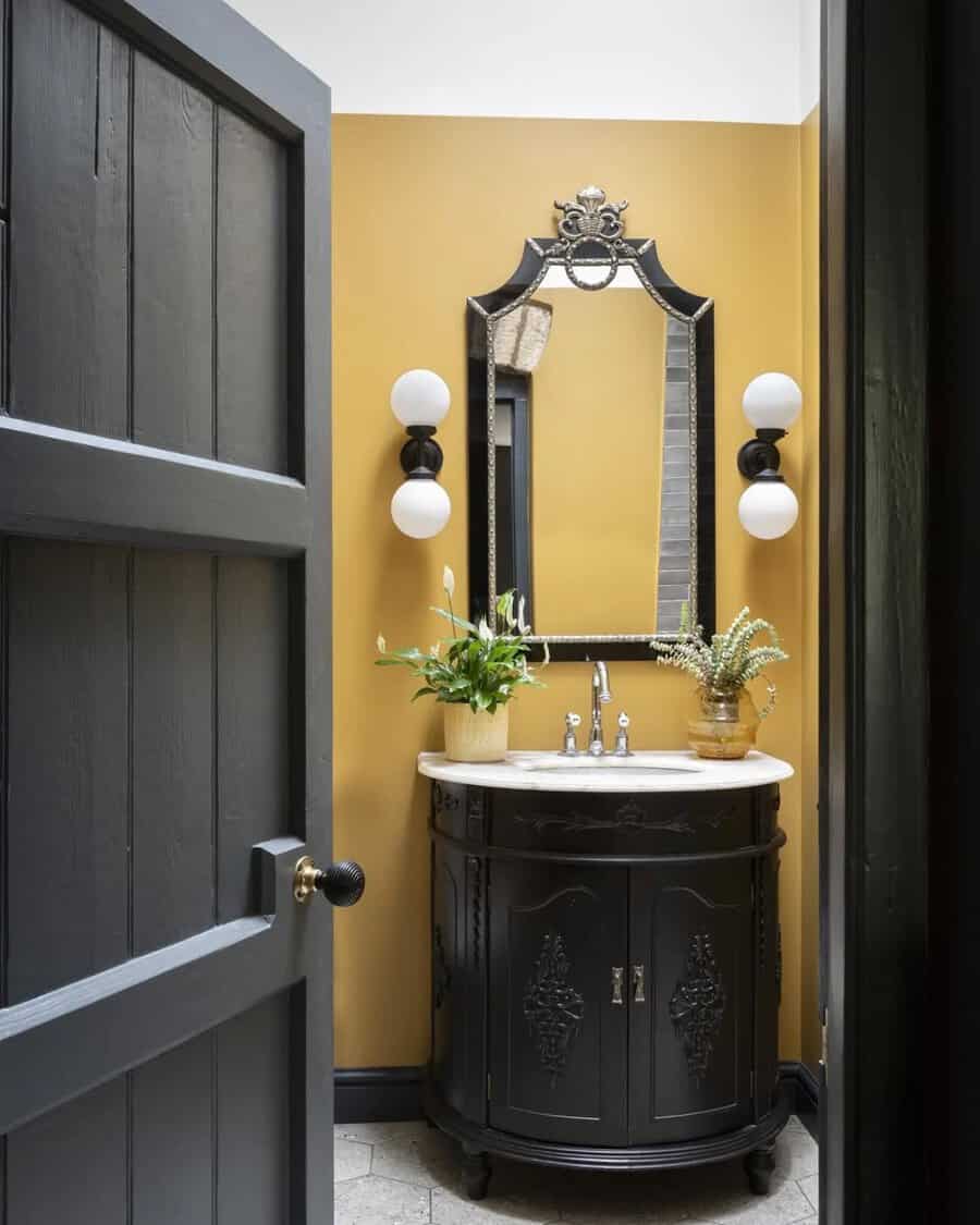 Bathroom with mustard yellow walls, black vanity, vintage mirror, and modern lighting for a classic, refined look.