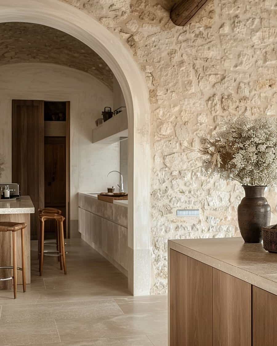 Spanish-style kitchen with a grand stone archway, textured walls, warm wood cabinetry, and a neutral-toned minimalist design.