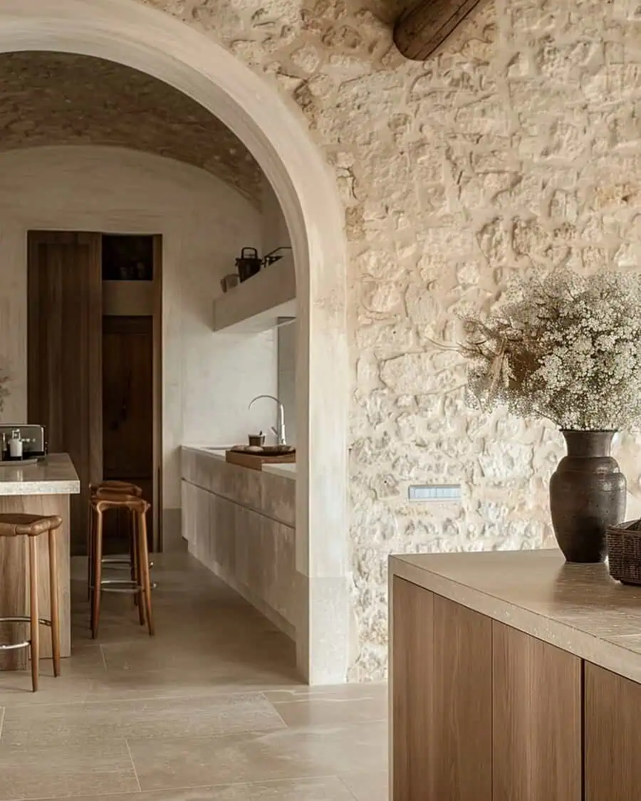 Spanish-style kitchen with a grand stone archway, textured walls, warm wood cabinetry, and a neutral-toned minimalist design.
