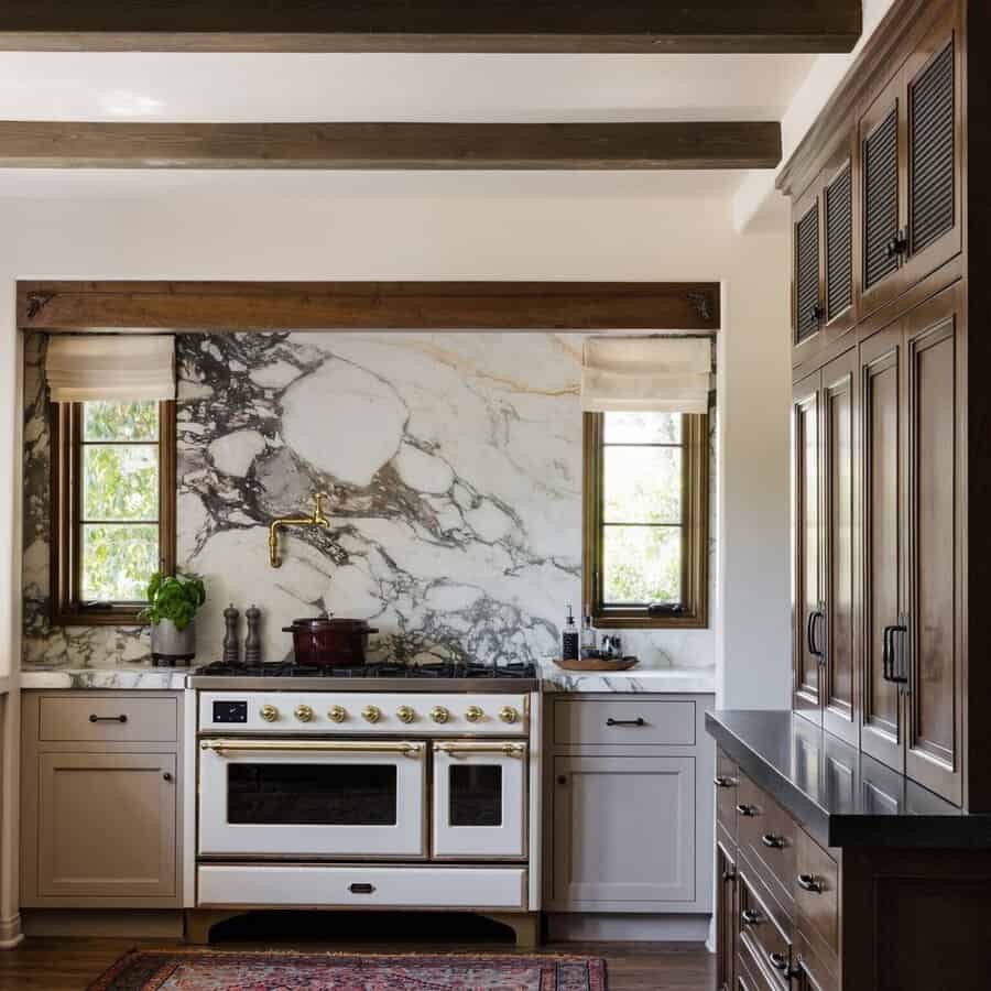 Spanish-style kitchen with wood beams, a marble backsplash, dark wood cabinetry, and a vintage-style range with brass accents.