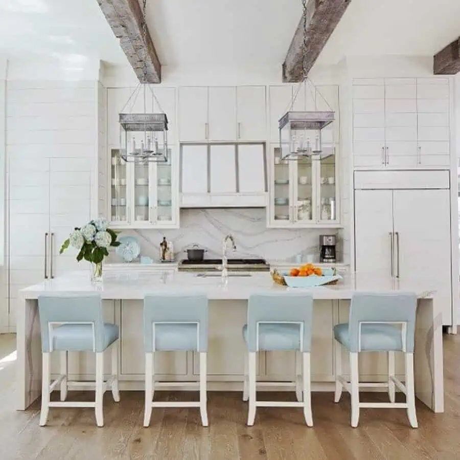Bright Spanish-style kitchen with natural light, white cabinetry, exposed beams, statement lanterns, and soft blue barstools.