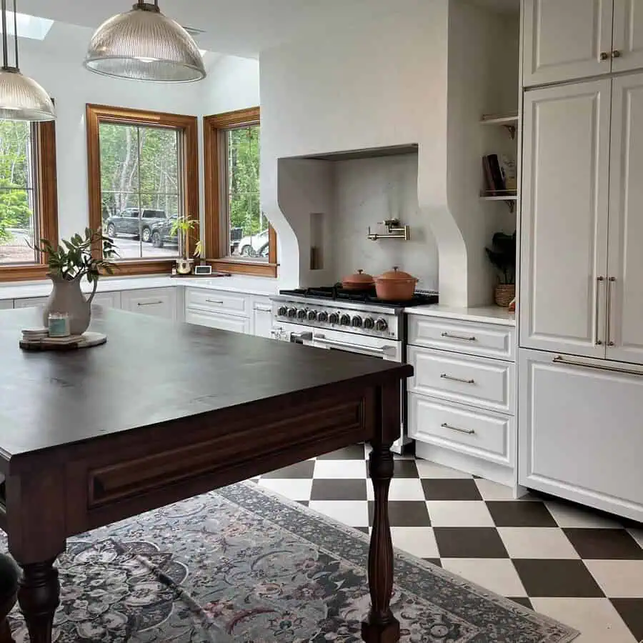Spanish-style kitchen with white paneled cabinets, gold hardware, a dark wood island, and a checkered tile floor.