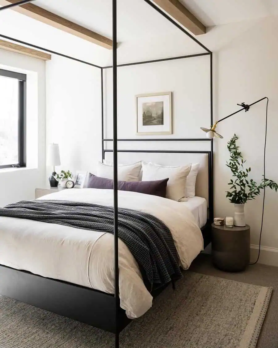 Black-framed canopy bed with neutral linens, soft accents, and a simple wall sconce in a serene, modern spare room.