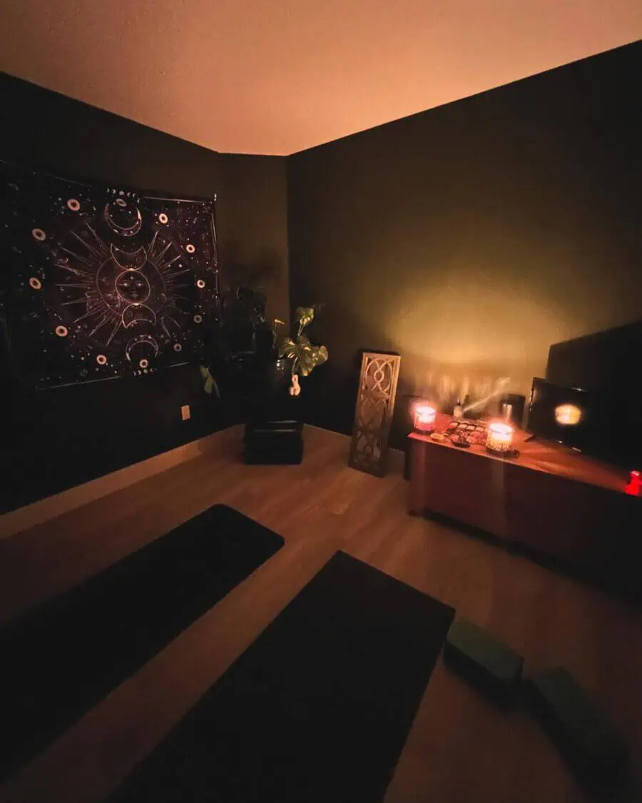 Dimly lit yoga room with dark walls, a tapestry, candlelight, and mats for a calm, introspective practice space.
