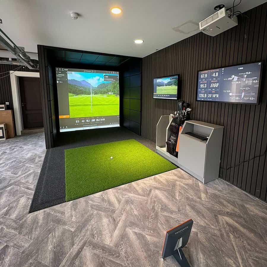 Garage converted into a sleek indoor golf simulator with monitors, turf flooring, and dark paneling for year-round practice.