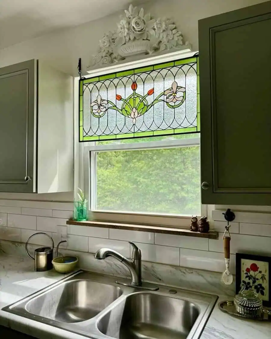 Kitchen sink with a stained glass panel above, white subway tile, and green cabinetry for a cozy, vintage-inspired look.