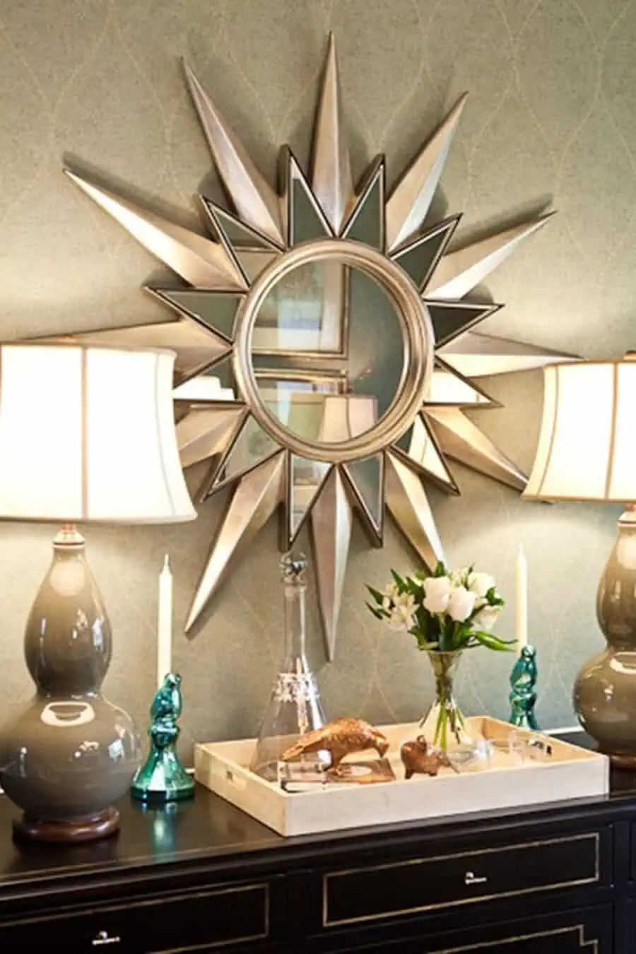 Starburst mirror above a console table with decorative lamps, flowers, and a styled tray.
