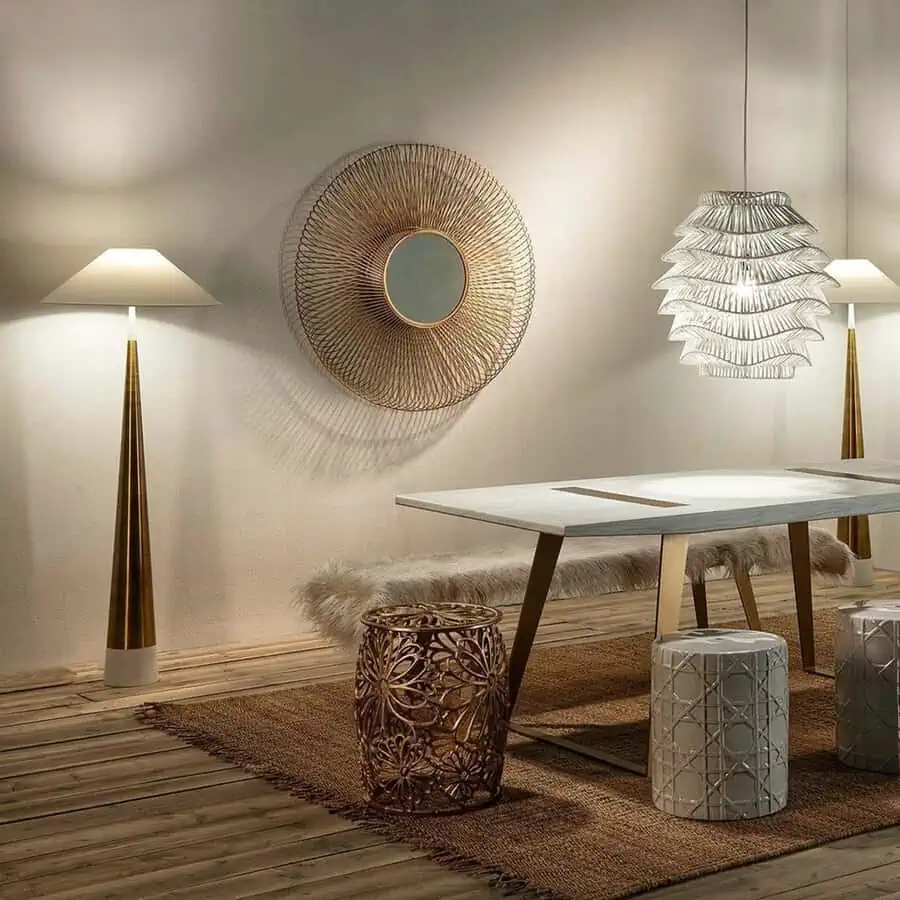 Round wire-frame mirror above a minimalist dining area with a white table, patterned stools, and sculptural lighting fixtures.