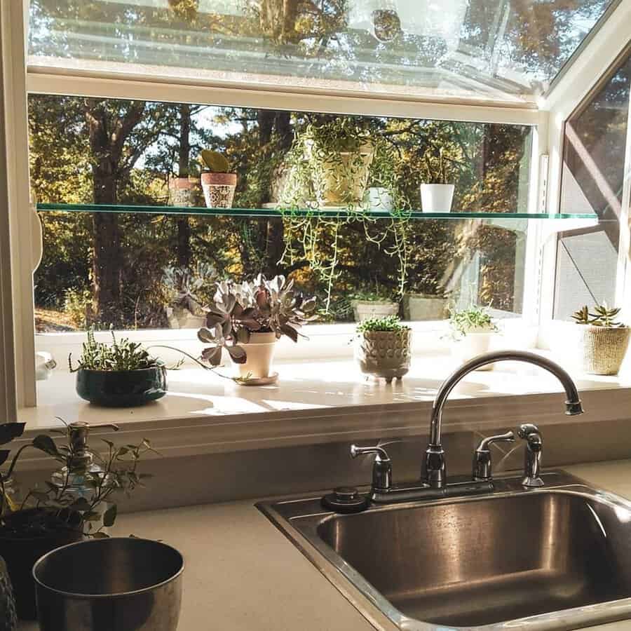 Kitchen greenhouse window with a glass shelf holding small potted plants above a stainless sink.