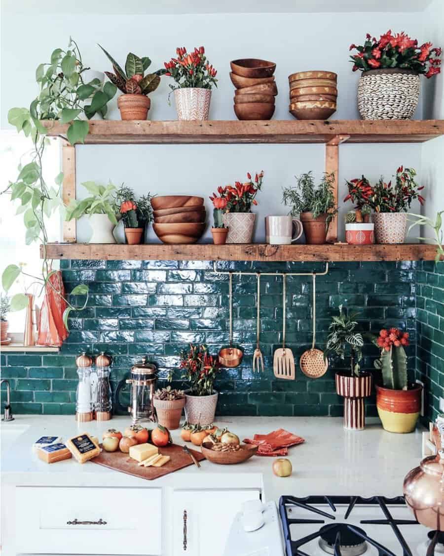 Spanish-style kitchen with deep green tile backsplash, rustic wood shelves, terra-cotta planters, copper accents, and colorful decor.