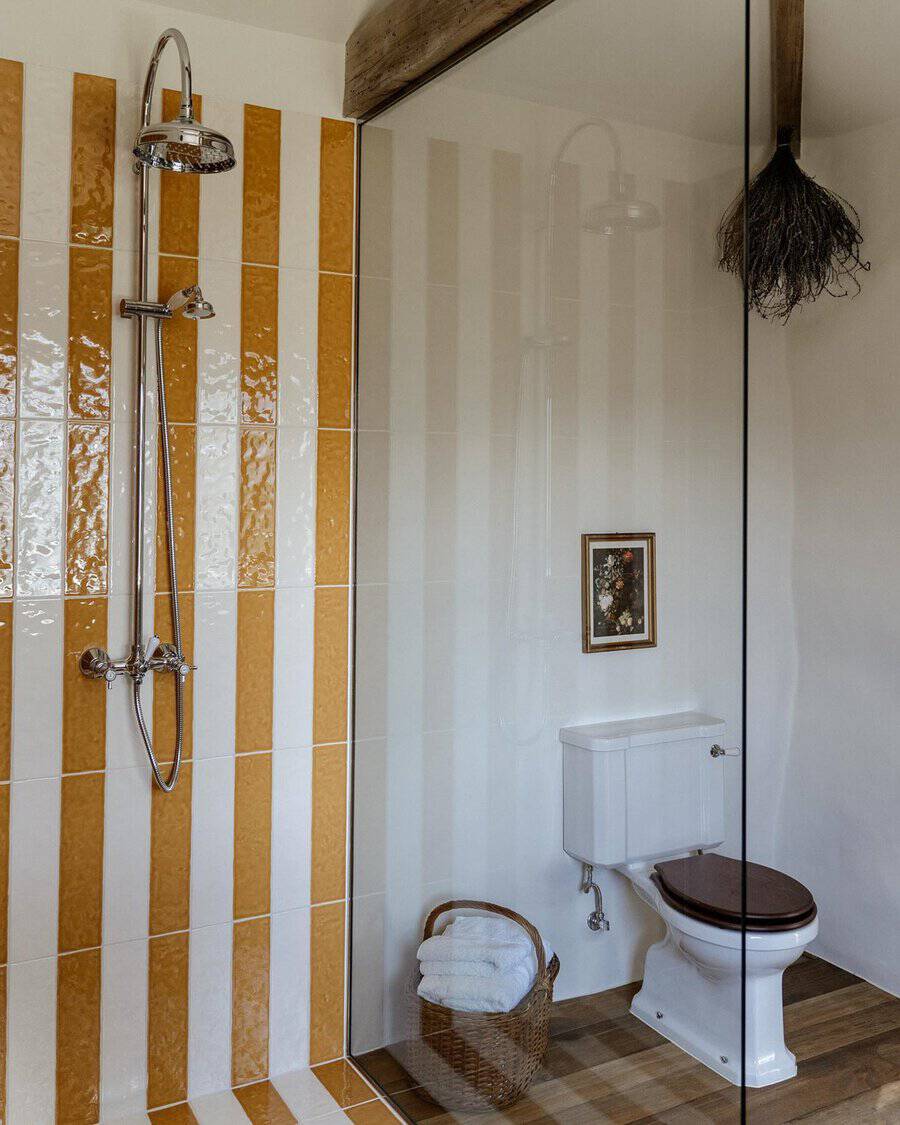 Bathroom with vertical striped tiles in yellow and white, a classic toilet, and a glass partition.
