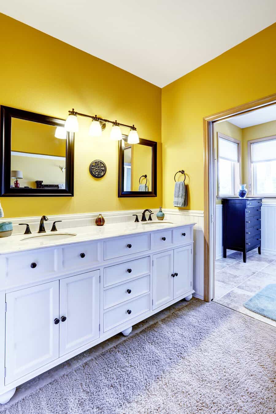 Yellow bathroom with a white vanity, dark-framed mirrors, and warm lighting creating a balanced, inviting space.