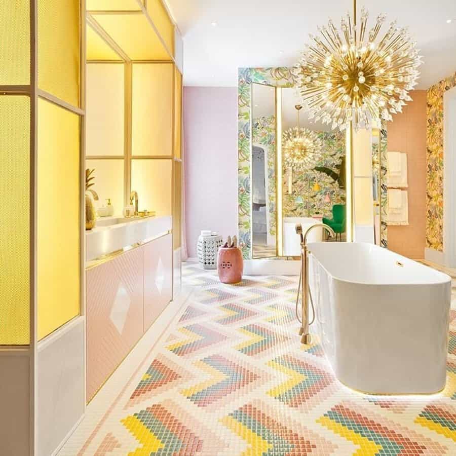 Bathroom with a pastel chevron tile floor, floral wallpaper, golden light fixtures, and a sleek white bathtub for a vibrant, luxurious design.