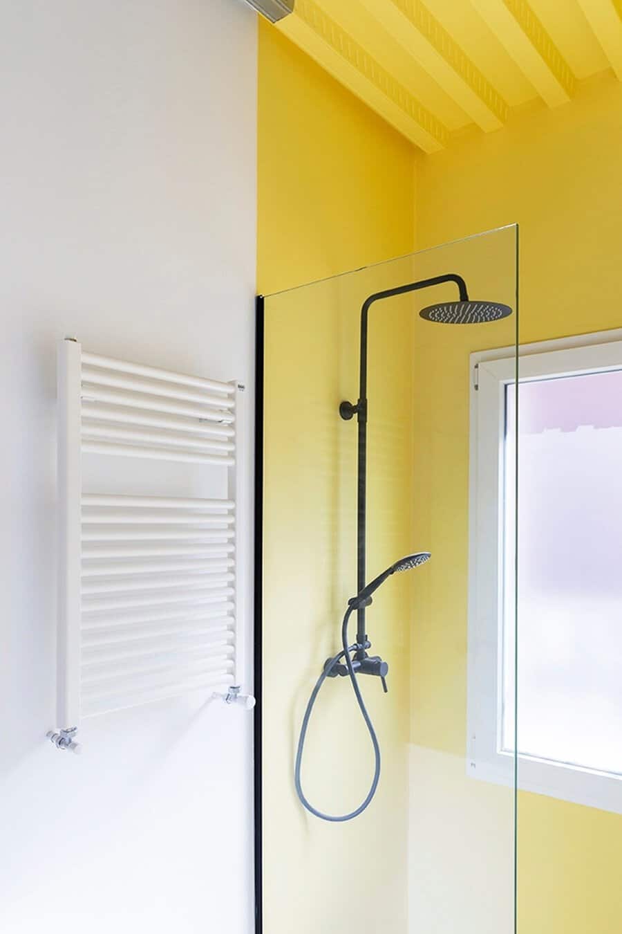 Minimalist shower with a bold yellow wall, black fixtures, and a glass partition for a modern and open design.