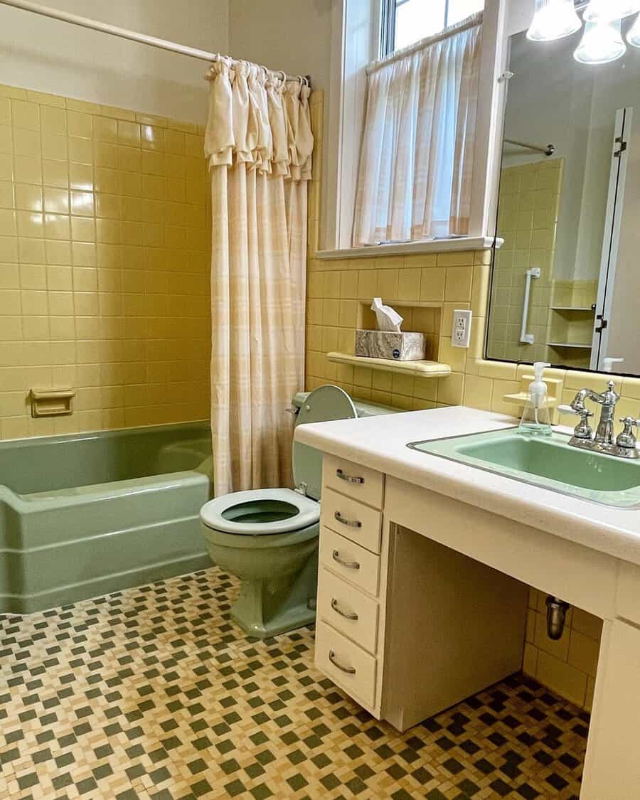 Retro bathroom with green and yellow tiles, vintage fixtures, floral curtains, and a classic checkered floor.