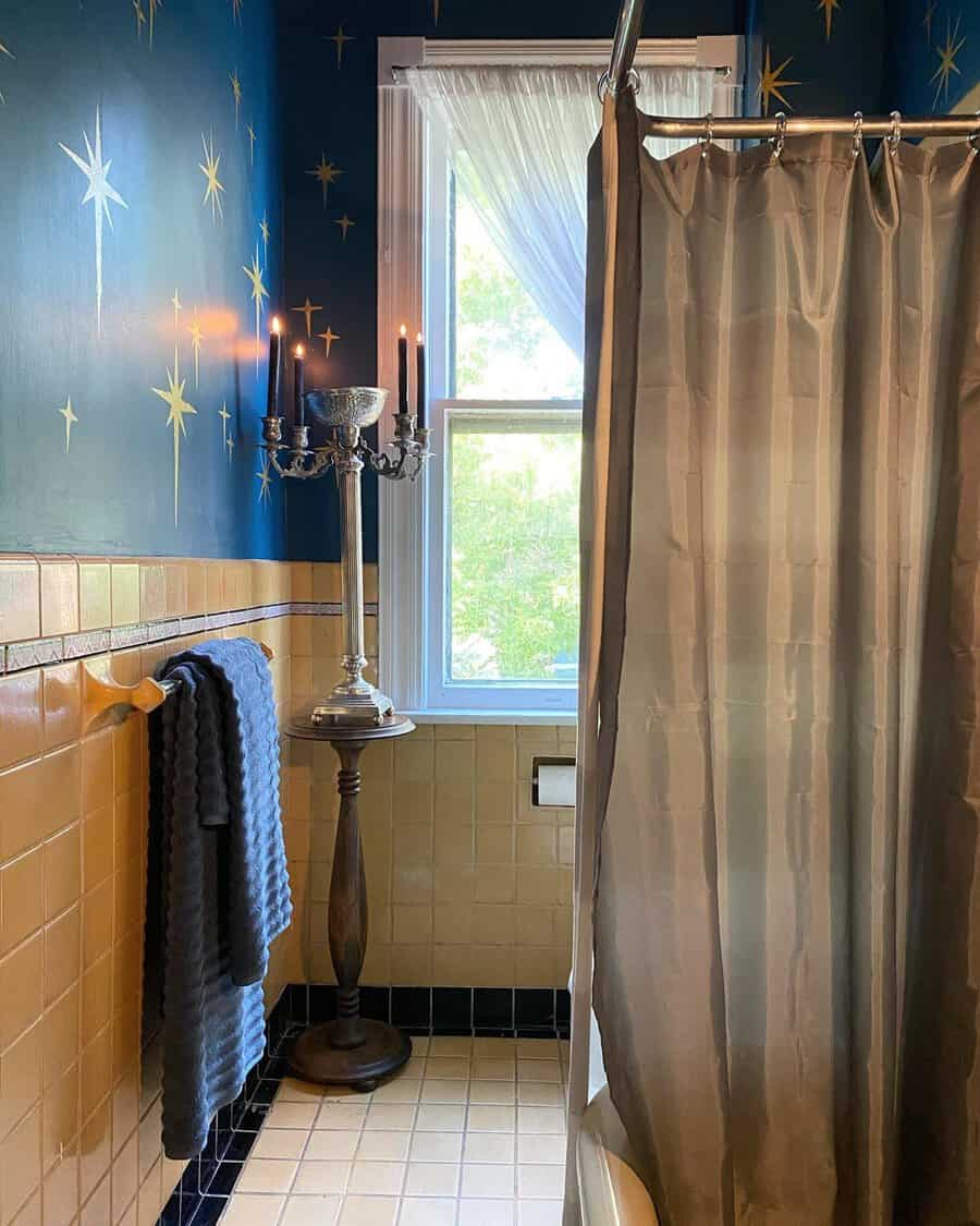 Bathroom with a starry accent wall, vintage candle stand, traditional tiles, and natural light for a cozy, classic atmosphere.