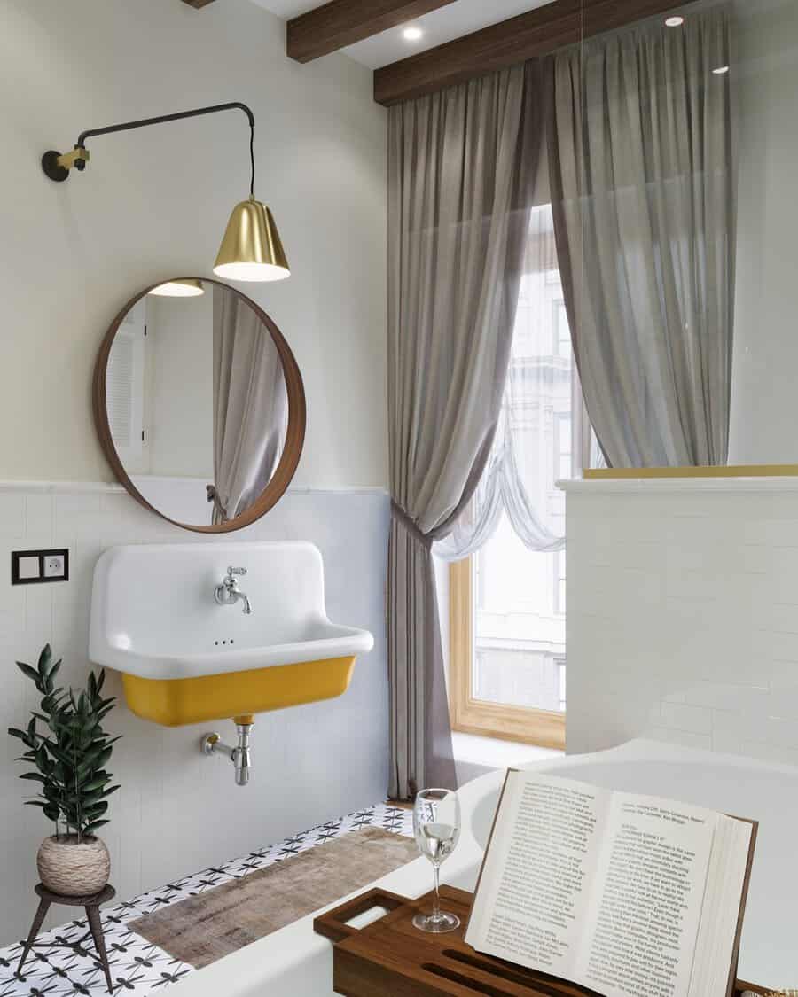 Bathroom featuring a white-and-yellow sink, round wood-framed mirror, gold sconce, and soft gray curtains for a warm, inviting look.