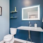 A small half bath with a lighted mirror modern sink and blue walls