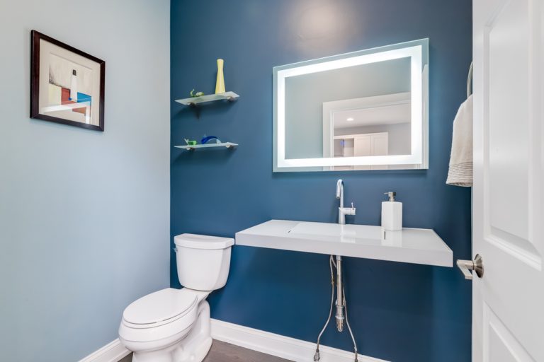 A small half bath with a lighted mirror modern sink and blue walls