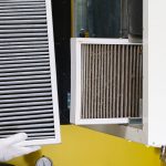 A gloved hand displays a clean air filter beside a dirty one being taken out of a ventilation unit