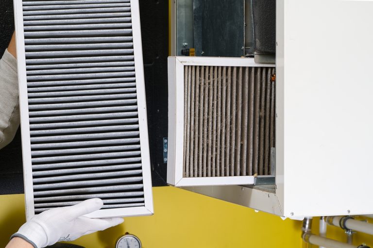 A gloved hand displays a clean air filter beside a dirty one being taken out of a ventilation unit